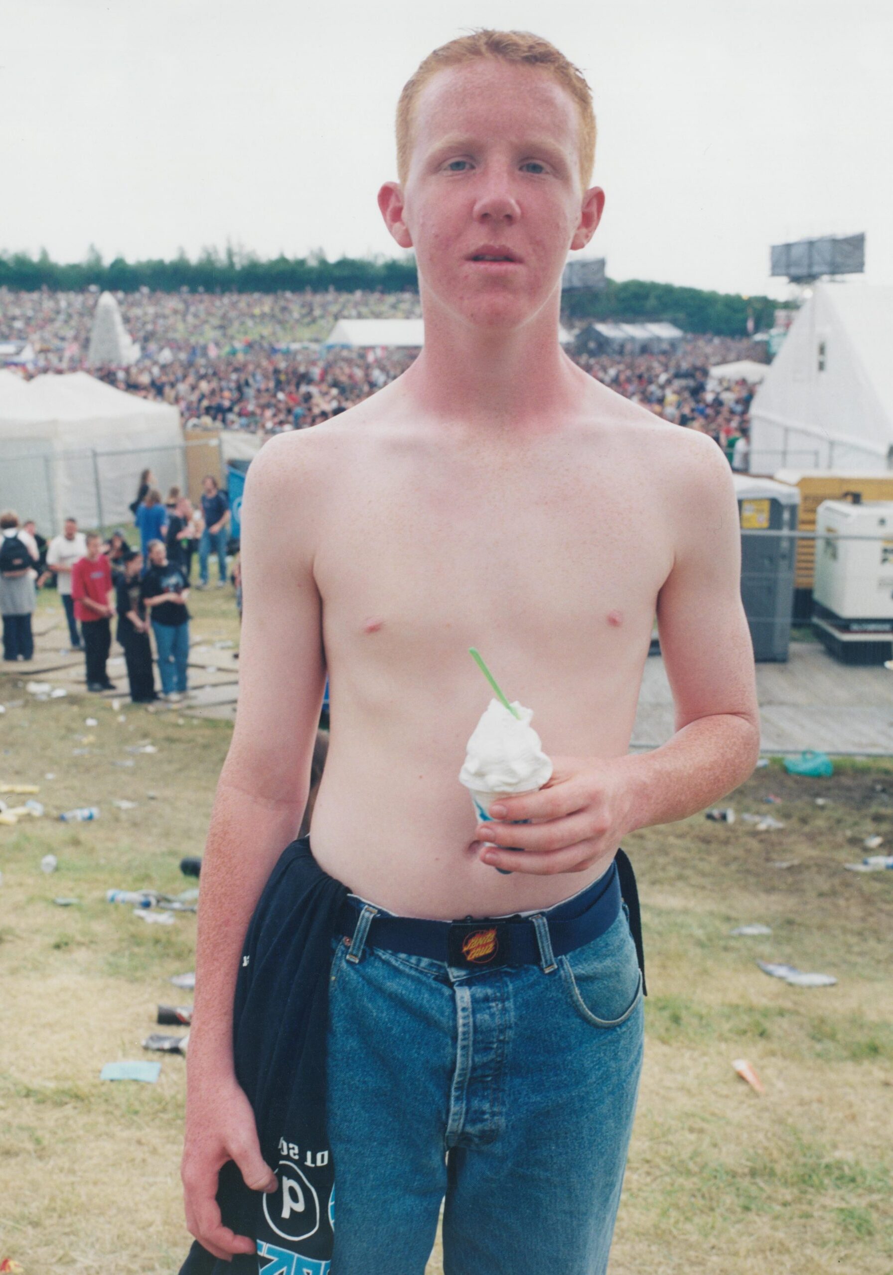 Young topless man holding a cup of ice cream and looking directly at camera. Teen eating an ice cream at Ozzfest, Milton Keynes Bowl, UK, 2001 by Rebecca Lewis