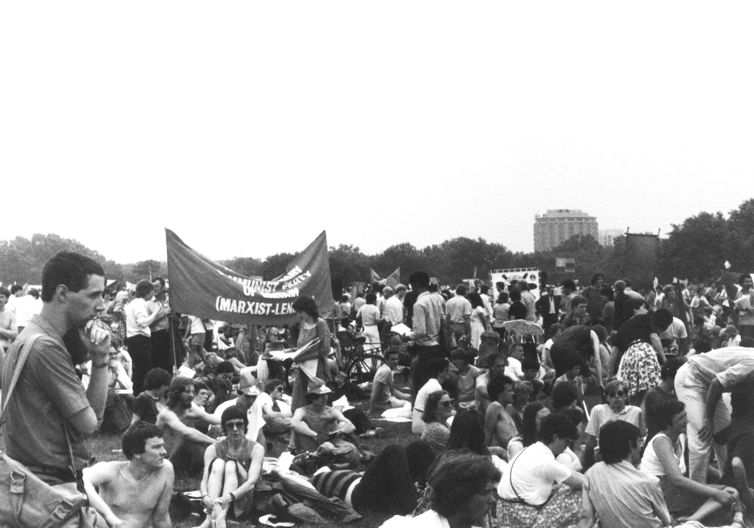 A seated crowd with a Communist Party banner. A large crowd seated around a Communist Party banner at a protest for nuclear disarmament, UK, 1980s.